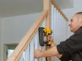 Mężczyzna montuje drewnianą balustradę schodową za pomocą zszywacza pneumatycznego.