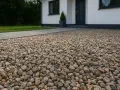 Zbliżenie na podjazd z żwiru o różnej wielkości i kolorze, obok domu.