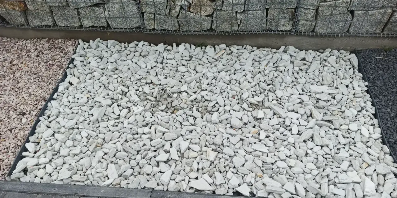 Biały grys na podjeździe obok gabionów i kostki brukowej.