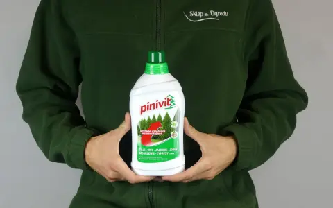 Osoba w zielonej bluzie trzyma butelkę **pinivit** – płynnego nawozu do roślin iglastych, wzmacniającego tuje, cisy i jałowce.