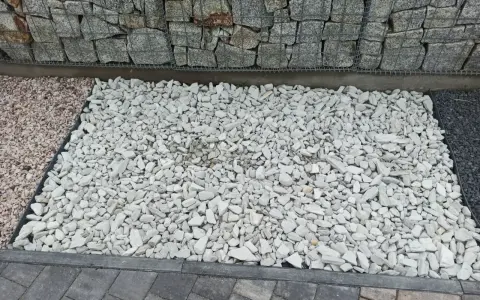 Biały grys na podjeździe obok gabionów i kostki brukowej.