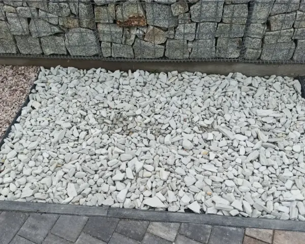Biały grys na podjeździe obok gabionów i kostki brukowej.