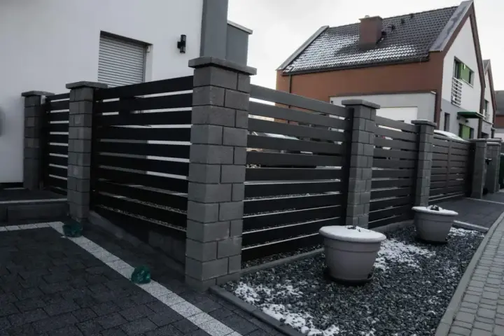 Nowoczesne ogrodzenie z betonowych słupków i ciemnych paneli. Taka wysokość ogrodzenia bez pozwolenia zapewnia prywatność.