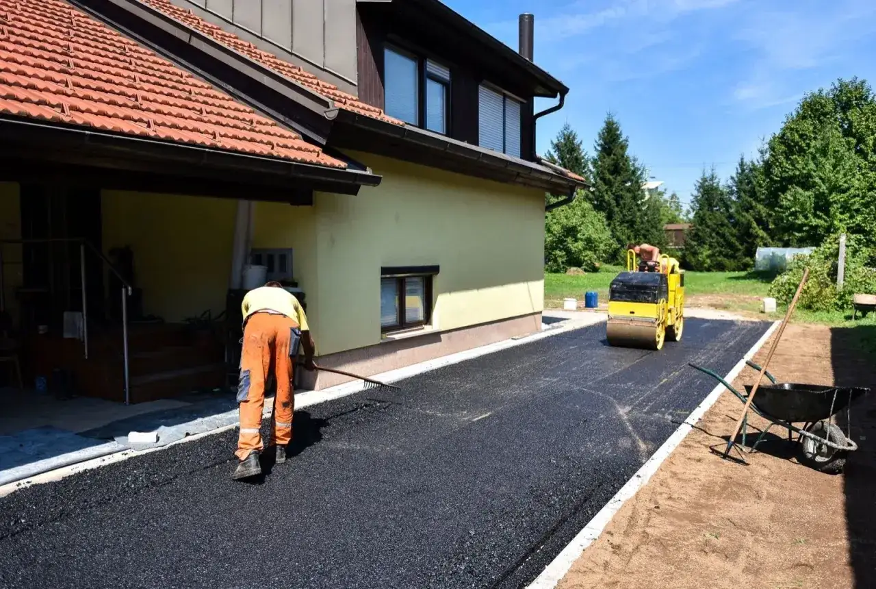 Pracownik równa asfalt na podjeździe, a walec go zagęszcza. Zastanawiasz się, ile kosztuje asfalt na podjazd?